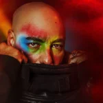 Roger Sanchez con la cara pintada de colores tapándose la boca con el cuello de la chaqueta
