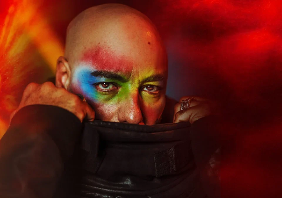 Roger Sanchez con la cara pintada de colores tapándose la boca con el cuello de la chaqueta