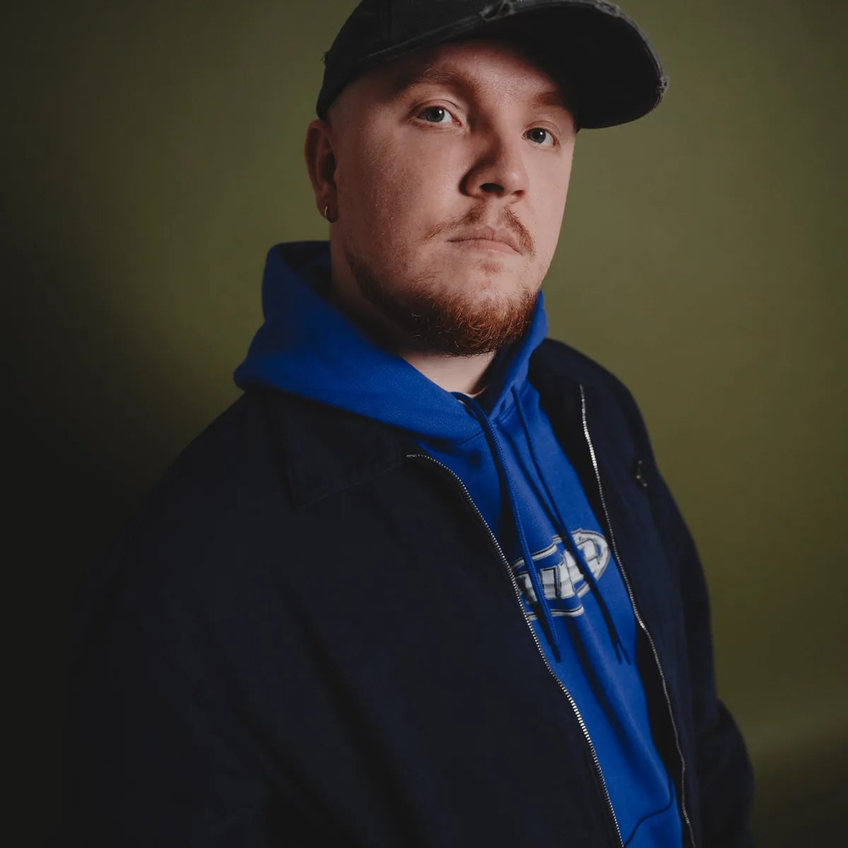 Retrato de prensa de Chris Stassy con gorra y sudadera azul